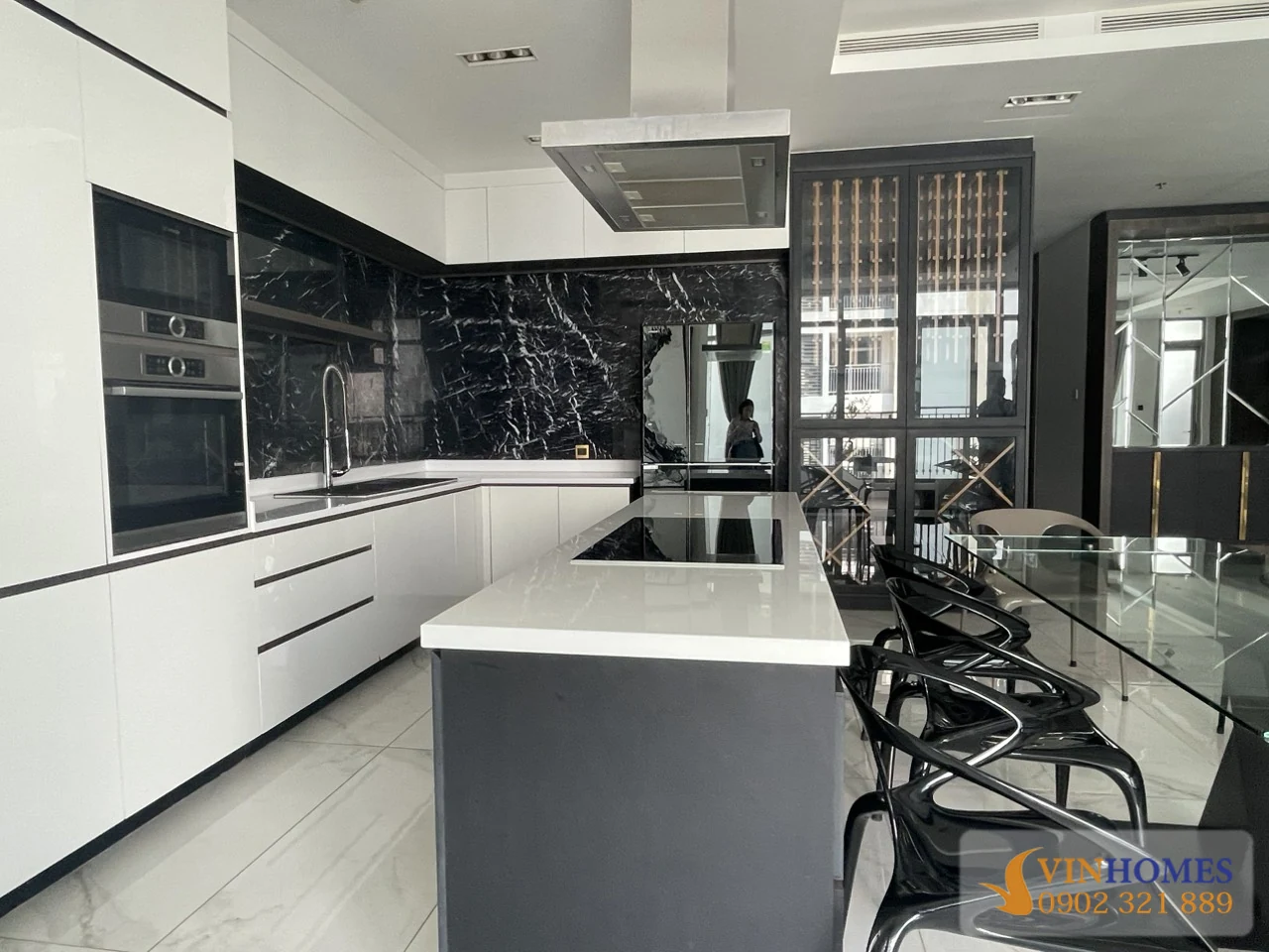 Khu bếp căn hộ Vinhomes Central Park với tủ bếp trắng, mặt đá đen và đảo bếp rộng