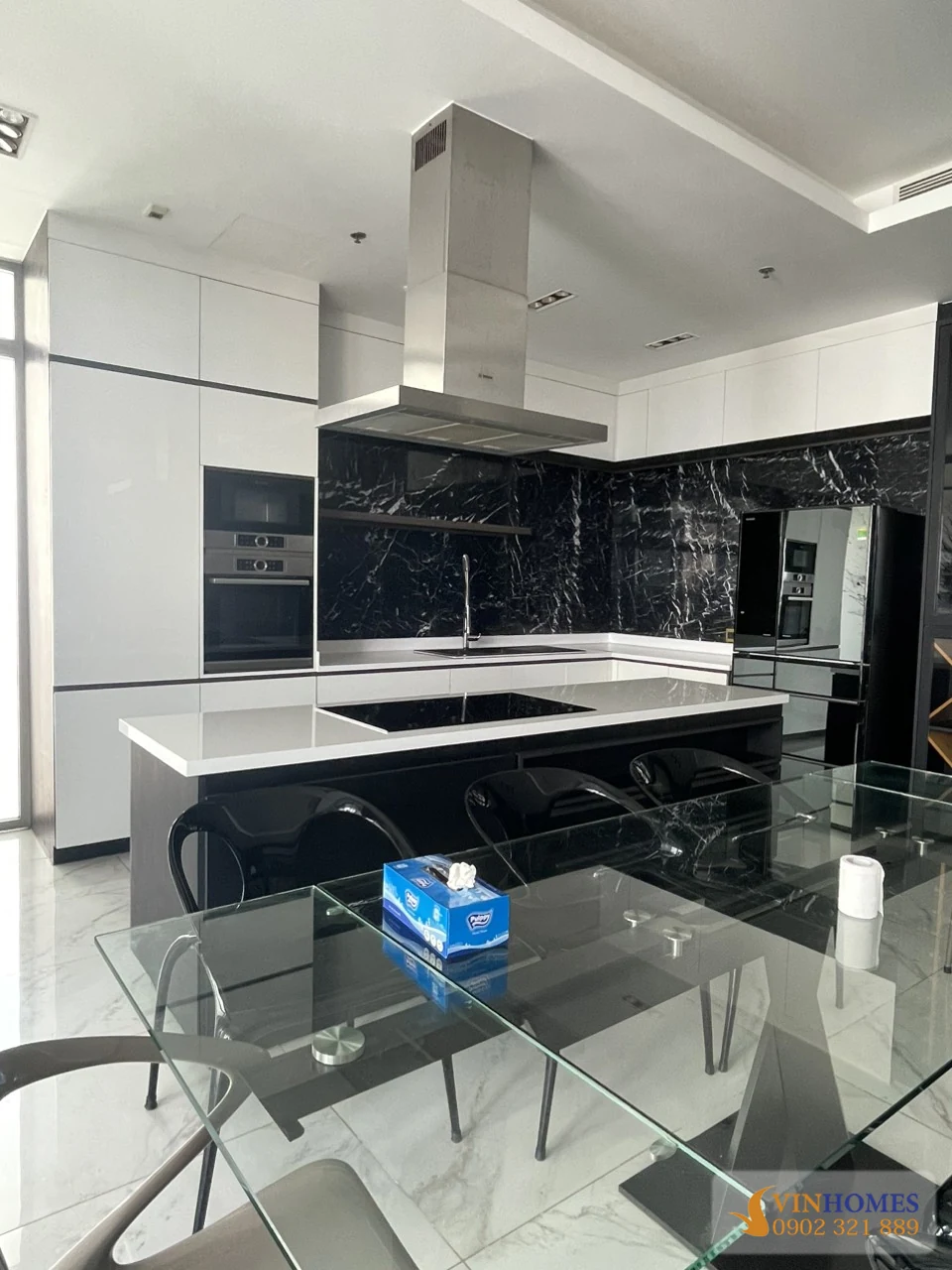Không gian bếp và bàn ăn căn hộ Vinhomes Central Park với đảo bếp, bàn kính và ghế hiện đại