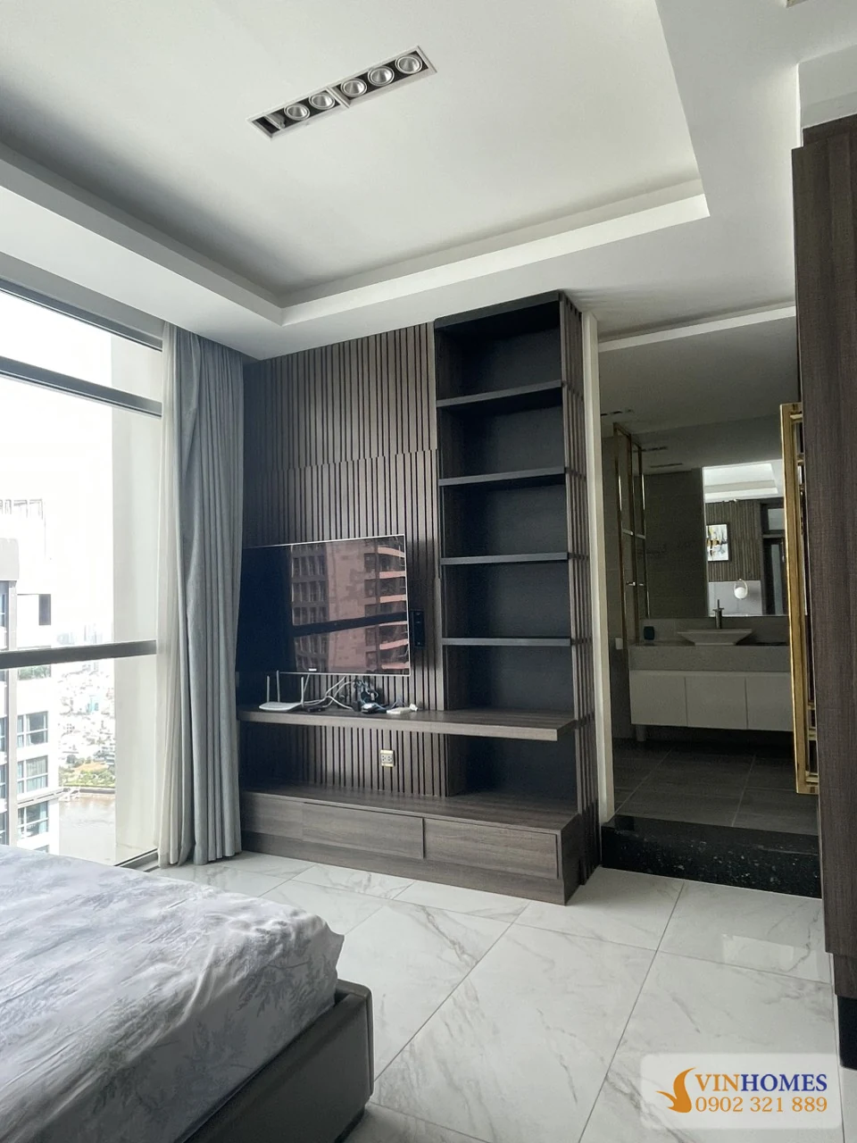 Phòng ngủ master căn hộ Vinhomes Central Park với kệ tivi âm tường và lối vào khu vệ sinh