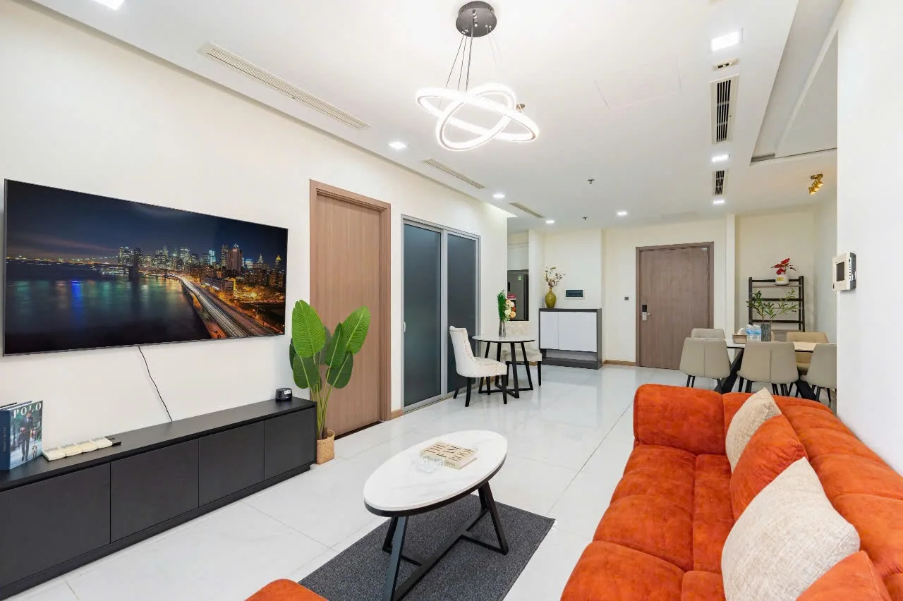 Phòng khách căn hộ Park 4 Vinhomes Central Park với TV treo tường, sofa cam và khu bàn ăn