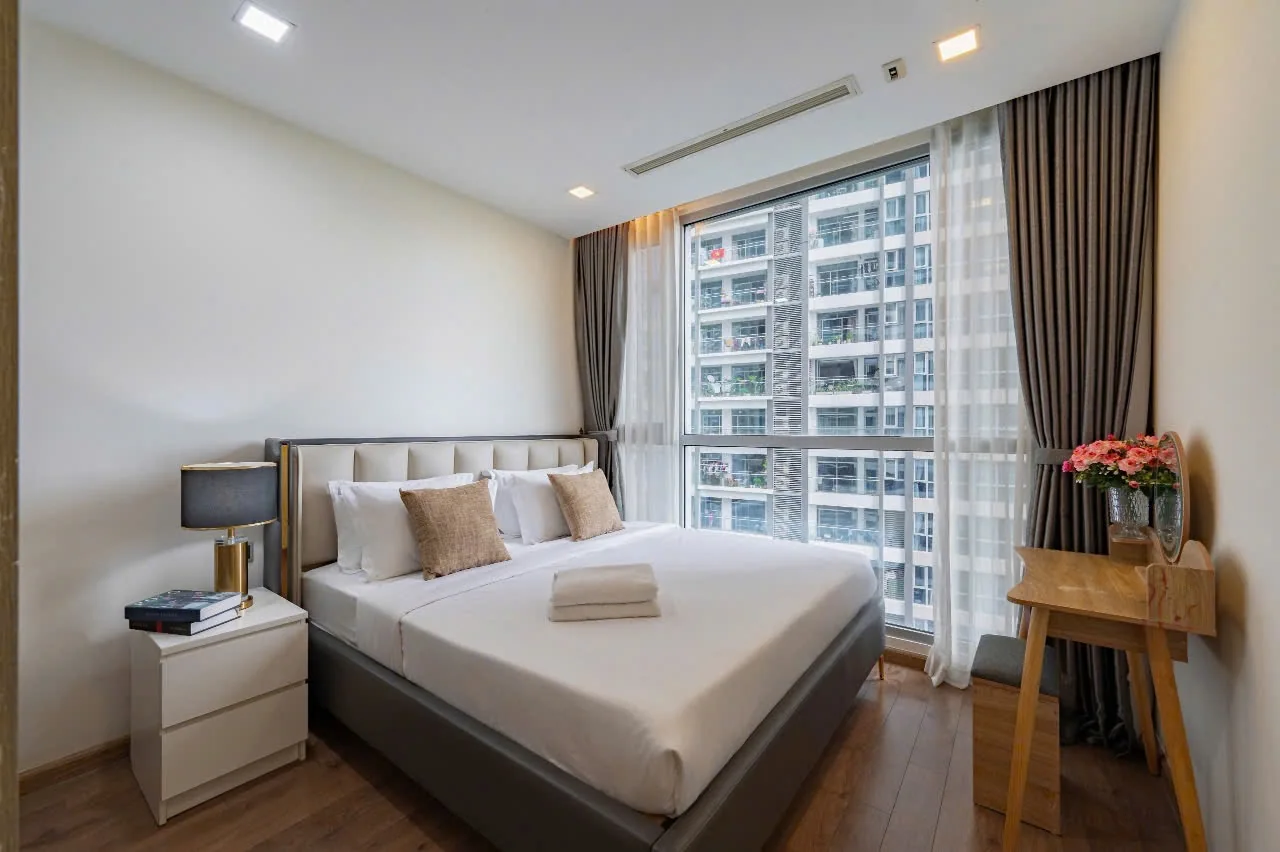 Phòng ngủ căn hộ Park 4 Vinhomes Central Park với cửa kính lớn, giường đôi và bàn trang điểm